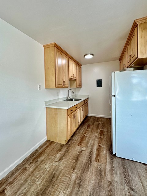an empty kitchen with wood flooring and a refrigerator